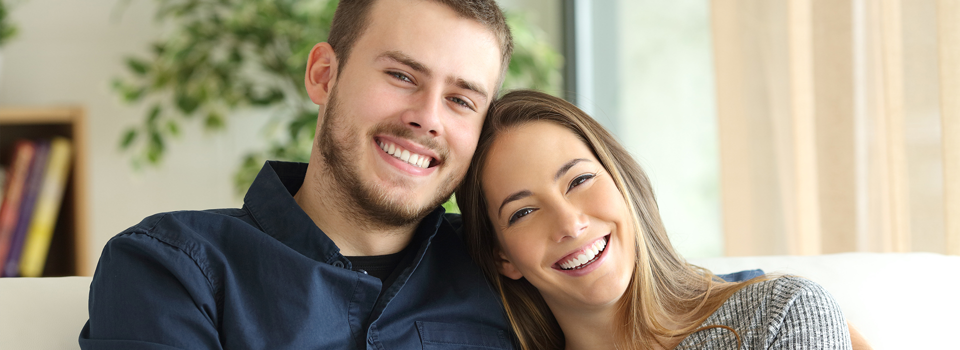 The image shows a man and a woman sitting closely together on a couch, smiling at the camera.