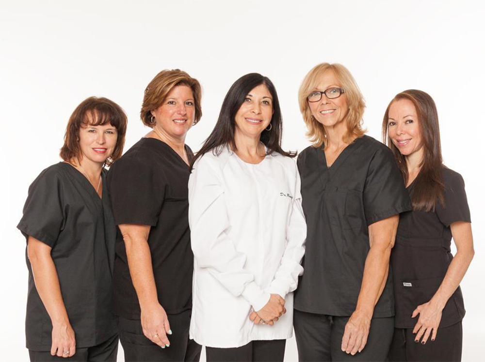 The image displays a group of six individuals, likely professionals given their attire, posing together for a portrait. They are all wearing scrubs and appear to be part of a healthcare team, possibly nurses or medical assistants, as indicated by the presence of stethoscopes.