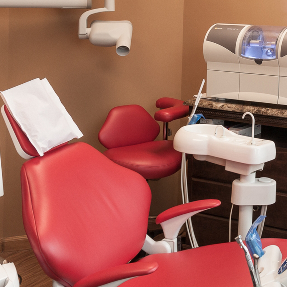 The image shows a dental office with a red chair, a dental machine, and a desk with a computer monitor.