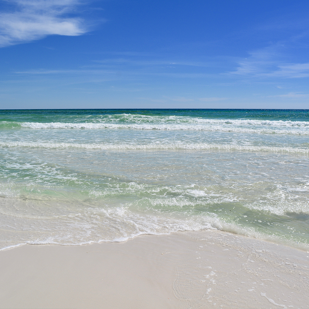 The image depicts a sandy beach with waves gently lapping against the shore, leading up to a clear blue sky.