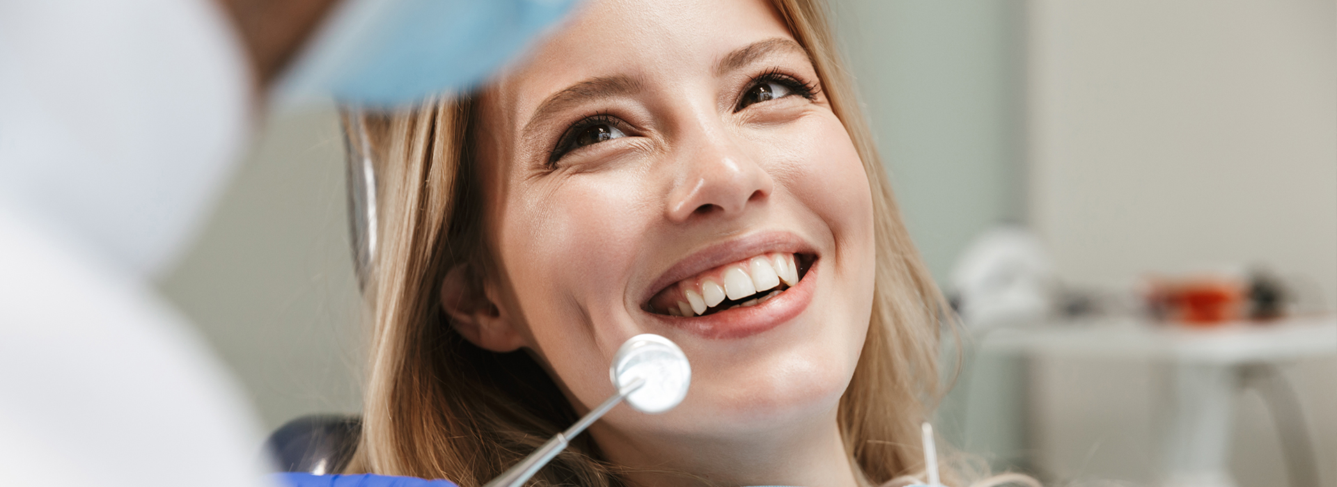 A woman with a smile is seen in the foreground, while a medical professional appears to be performing a procedure or examination on her teeth.