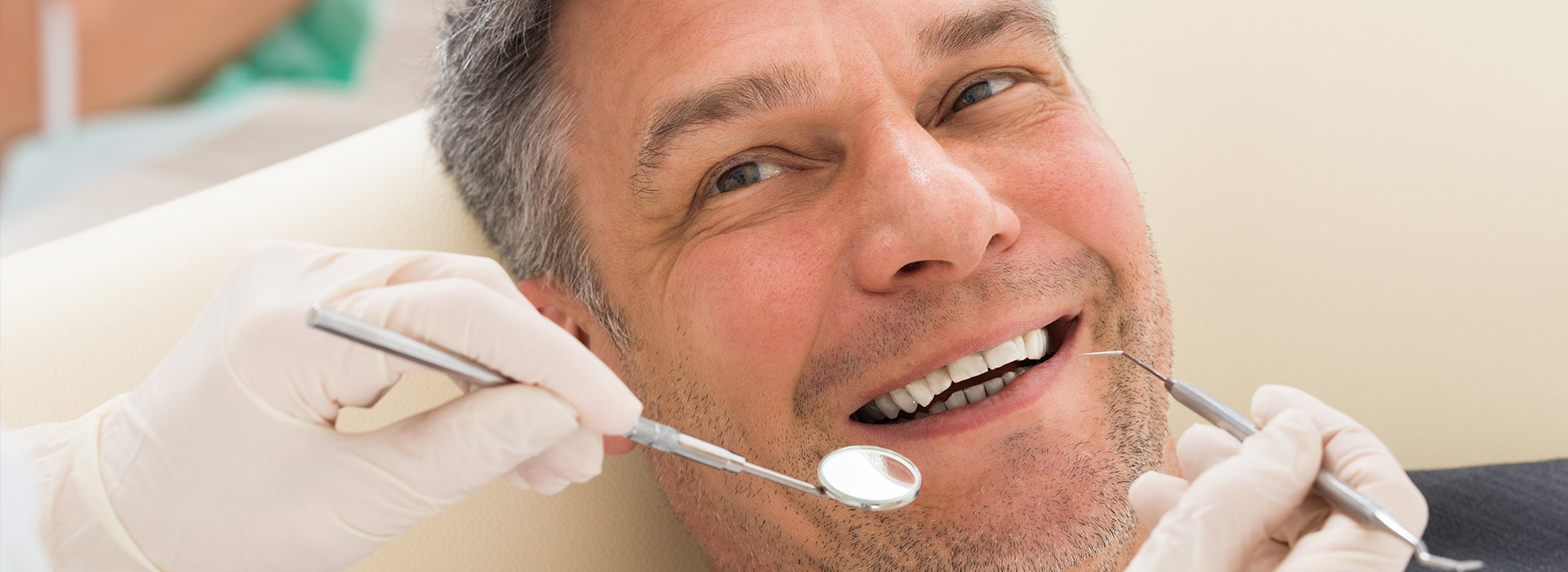 A man is sitting in a dental chair, receiving dental care with his mouth open and teeth visible.
