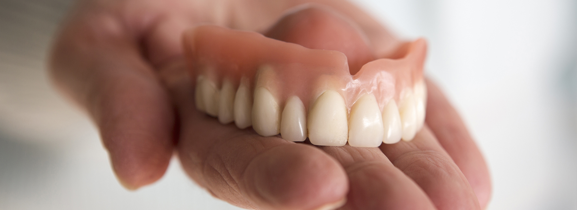 The image shows a person holding a set of dentures with their left hand, displaying the upper and lower parts of the artificial teeth.