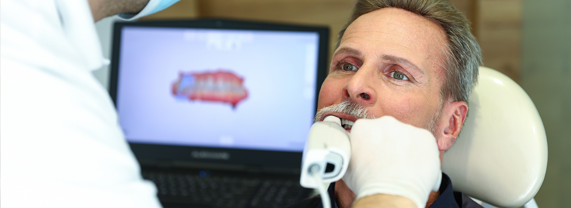 The image shows a person receiving dental care, with a dentist performing an examination or treatment using a computer-assisted device.
