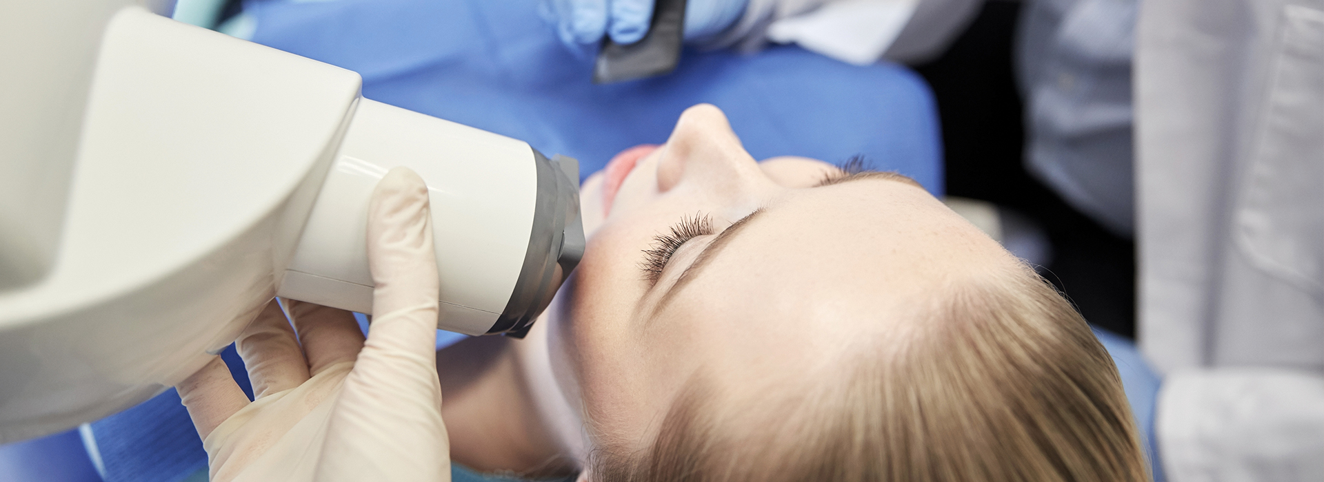A person is seated in a dental chair, receiving dental care with a dentist performing an examination using a magnifying device.