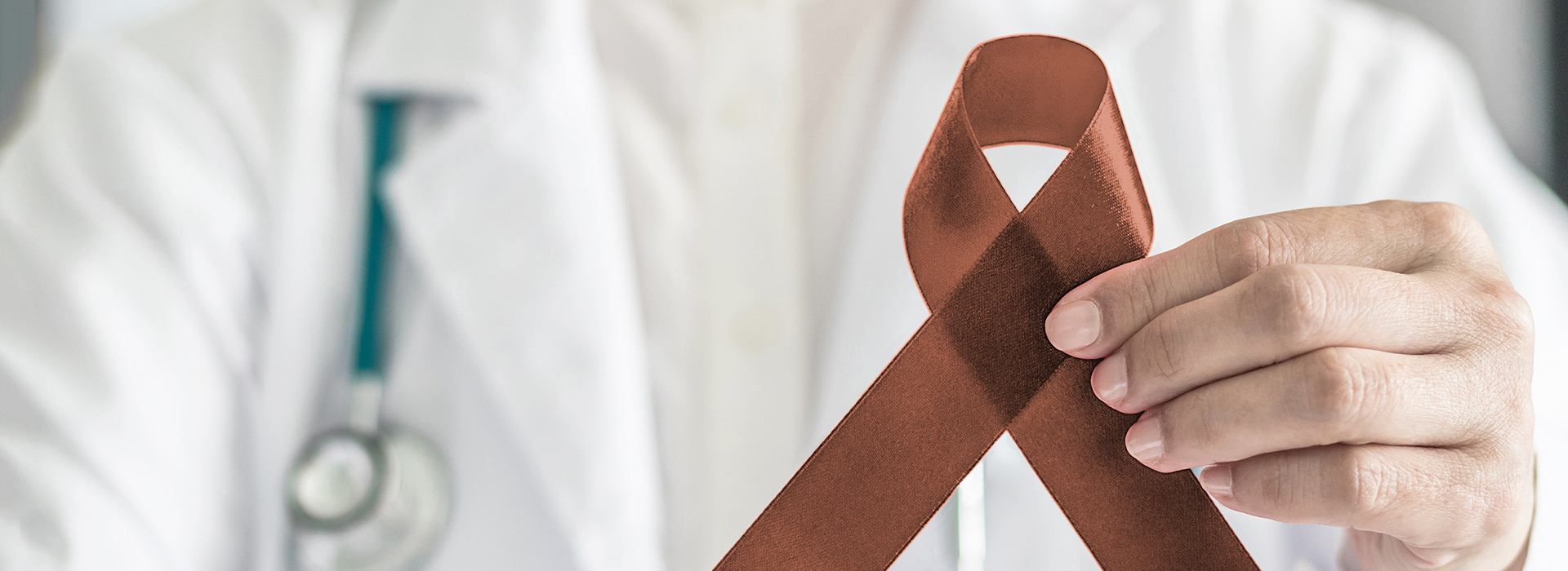 The image shows a medical professional, presumably a doctor or nurse, holding up a red ribbon with a brown band around it.