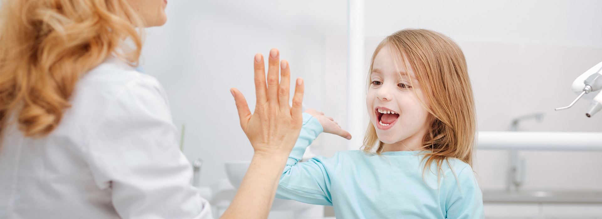 A woman and a young girl are in a bathroom, with the girl standing on a chair to reach the sink.