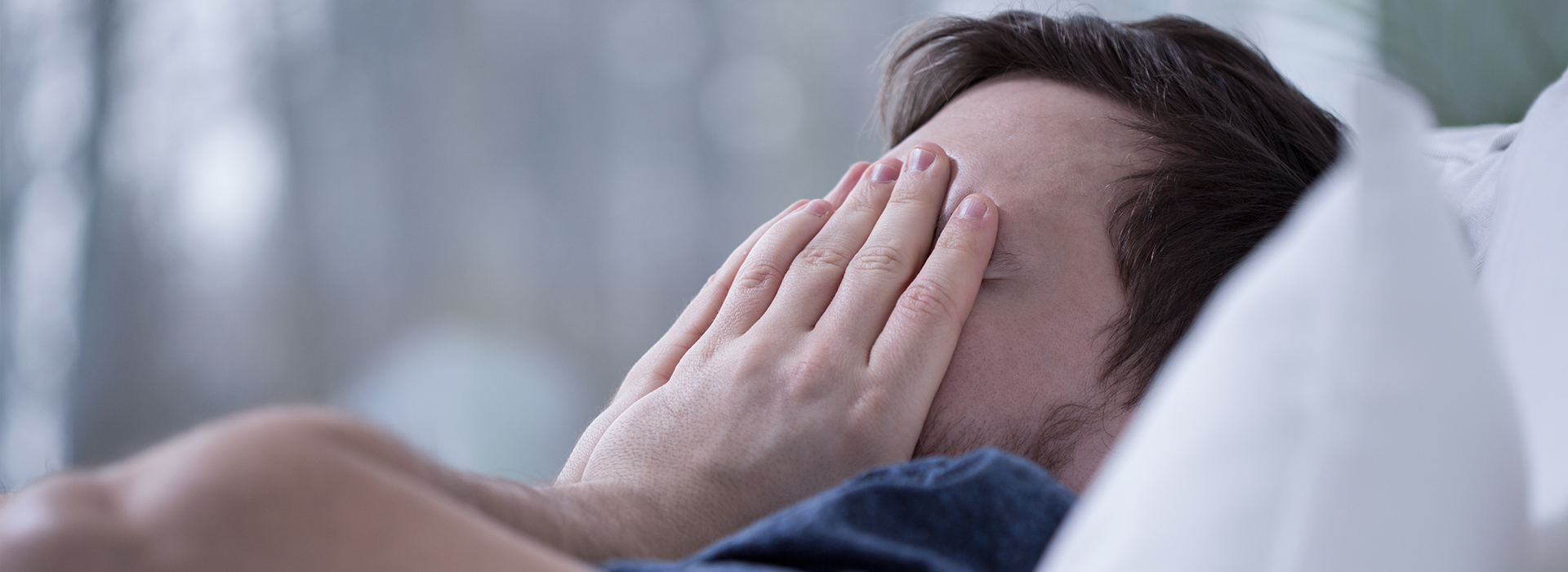 A person lying in bed with their hands covering their face, appearing to be asleep or resting.