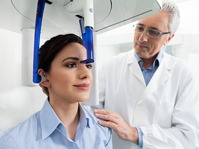 The image shows a woman seated in a dental chair, wearing a blue headgear, with a dentist standing behind her, both in a dental office setting.