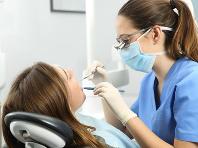 A dental hygienist performing a procedure on a patient in a dental office setting.