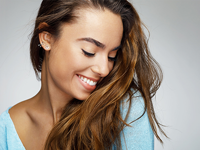 A woman with long hair, smiling and looking down slightly.