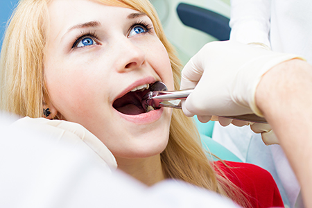 A woman receiving dental care, with a dentist holding a drill and working on her teeth.