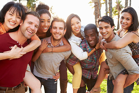 A group of young adults posing joyfully for a photo outdoors, smiling and embracing each other.