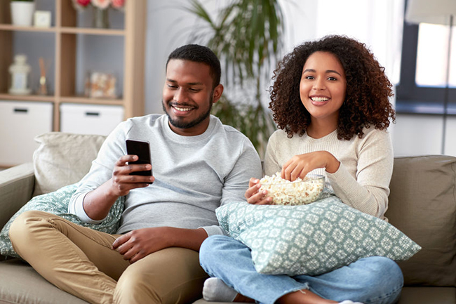 A man and a woman sitting on a couch, sharing a moment while watching something on a cell phone.