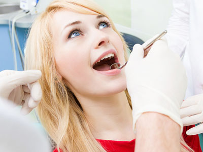 The image shows a woman receiving dental care, with a dentist performing a procedure on her teeth while she is seated in a dental chair.