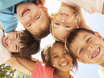 A joyful group of children, both boys and girls, smiling at the camera from different angles.